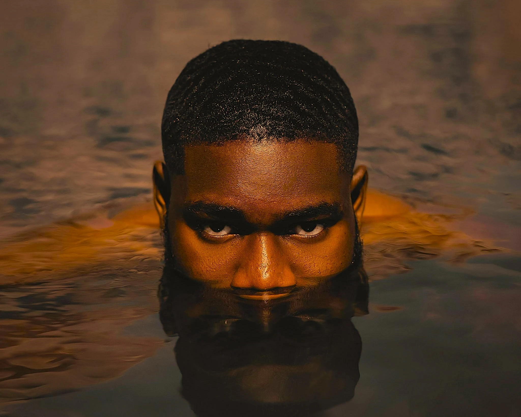 A photo of a guy in a pool of water, with the body submerged in the water